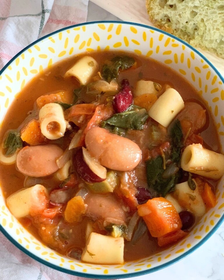 Close-up look of Minestrone Soup served in a bowl, seen in the background, is some chutney-spiced focaccia.