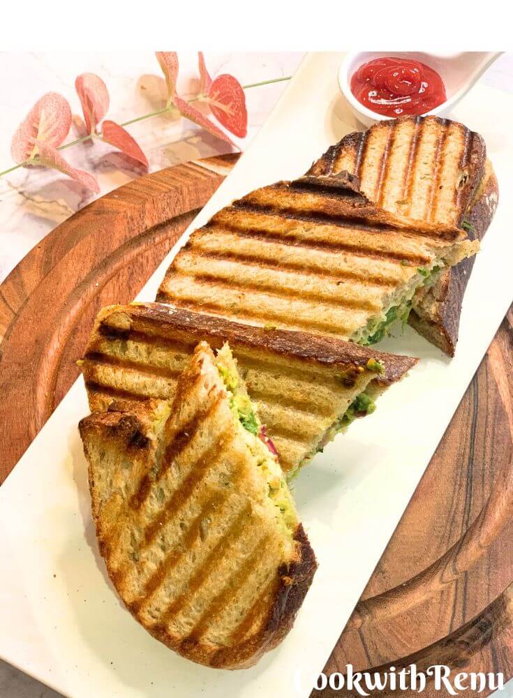 2 Sandwich pieces served on a white plate on brown cheese boards. The sandwich is served along with tomato ketchup.