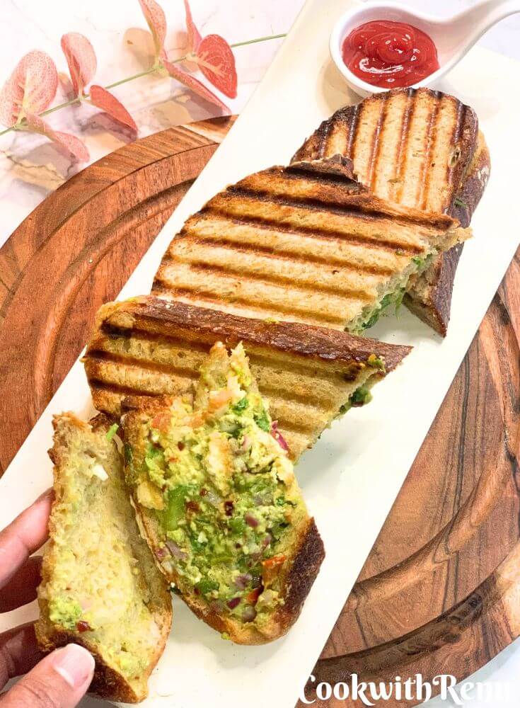 A Veg sandwich is seen in a slice, along with a few more sandwich slices seen in the white plate.