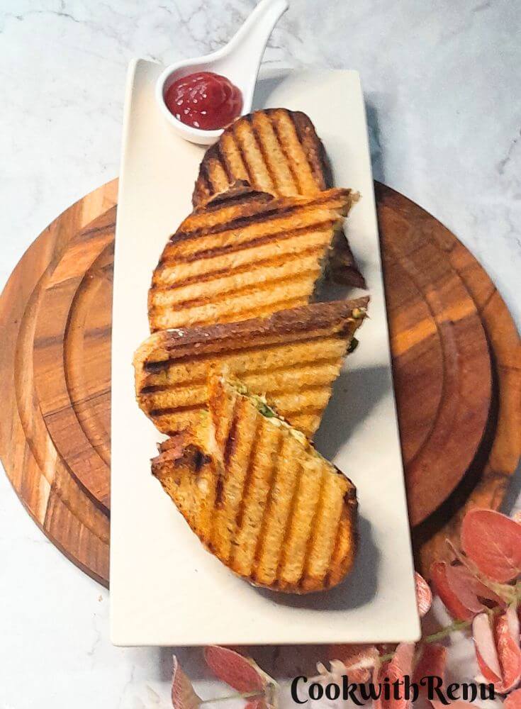 2 Sandwich pieces served on a white plate on brown cheese boards. The sandwich is served along with tomato ketchup.