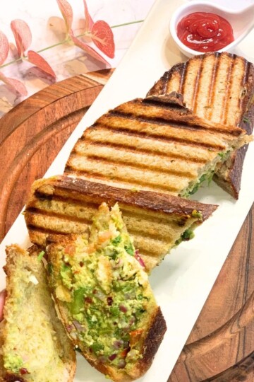 A Veg sandwich is seen in a slice, along with a few more sandwich slices seen in the white plate.