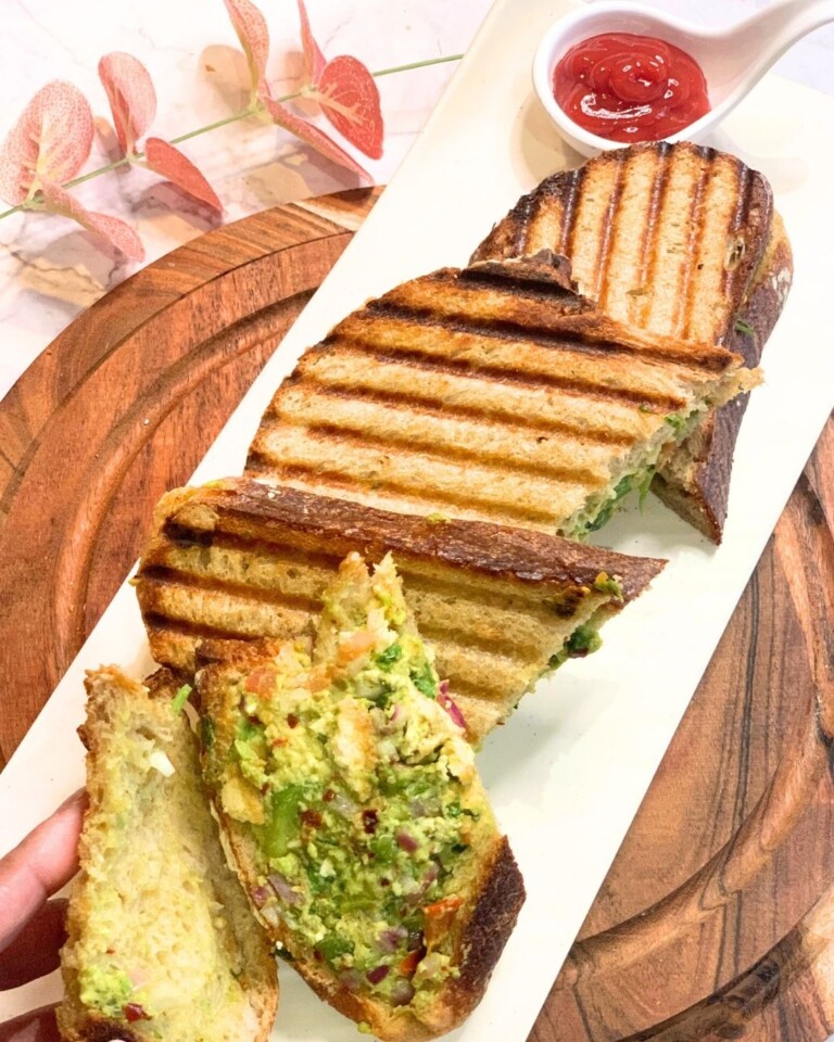 A Veg sandwich is seen in a slice, along with a few more sandwich slices seen in the white plate.