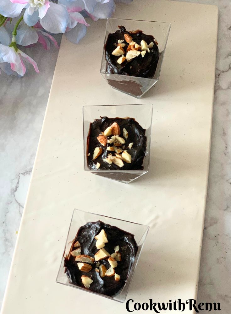 3 small Avocado Chocolate Mousse dessert cups served on a white plate, with artificial flowers in the background.