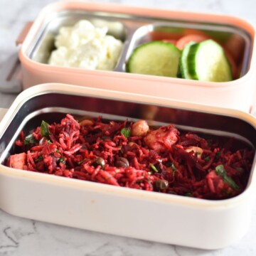 Beetroot Paneer Rice served in a lunchbox along with some cucumber, tomato, and yogurt.