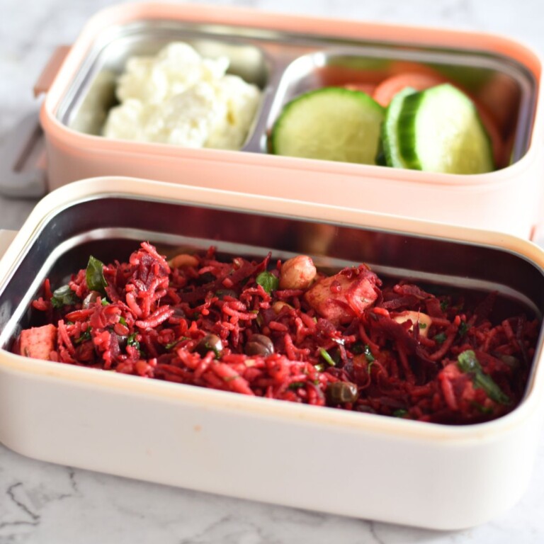 Beetroot Paneer Rice served in a lunchbox along with some cucumber, tomato, and yogurt.