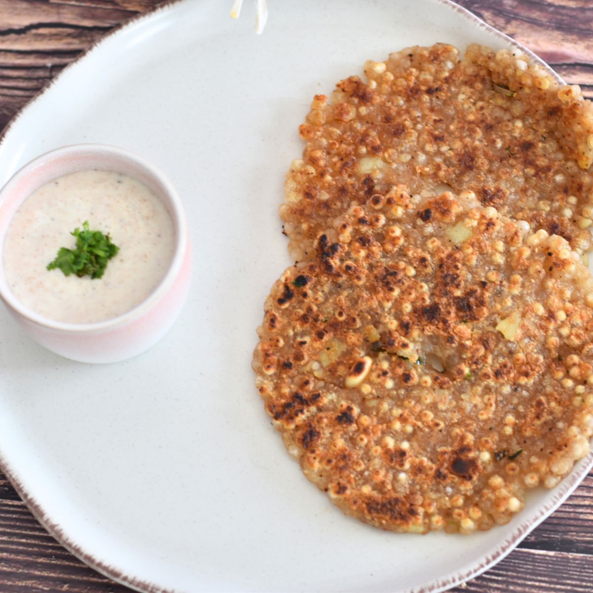 Sabudana Thalipeeth served on a white plate with peanut yogurt raita.