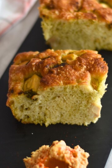 No-Knead Green Chutney Focaccia With Tofu served on a black board with hummus on the side.