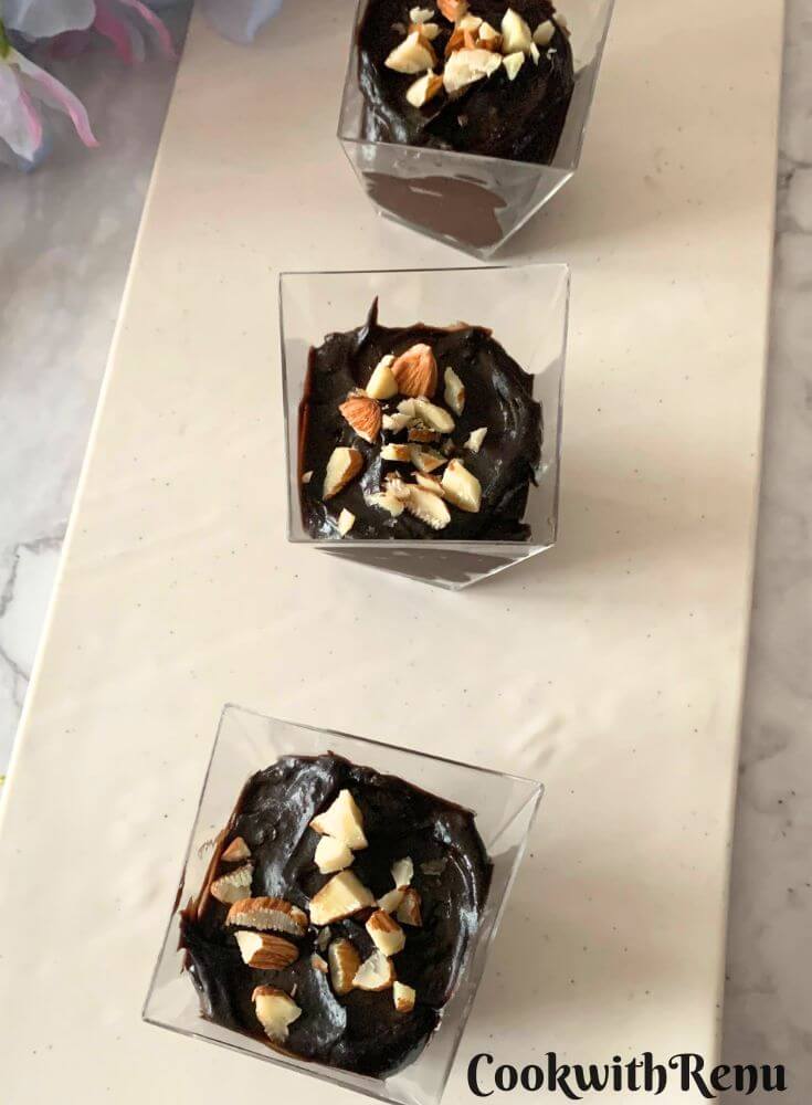 Small portions of Avocado Chocolate Mousse served in disposable cups, ready for the party, are arranged on a white tray.