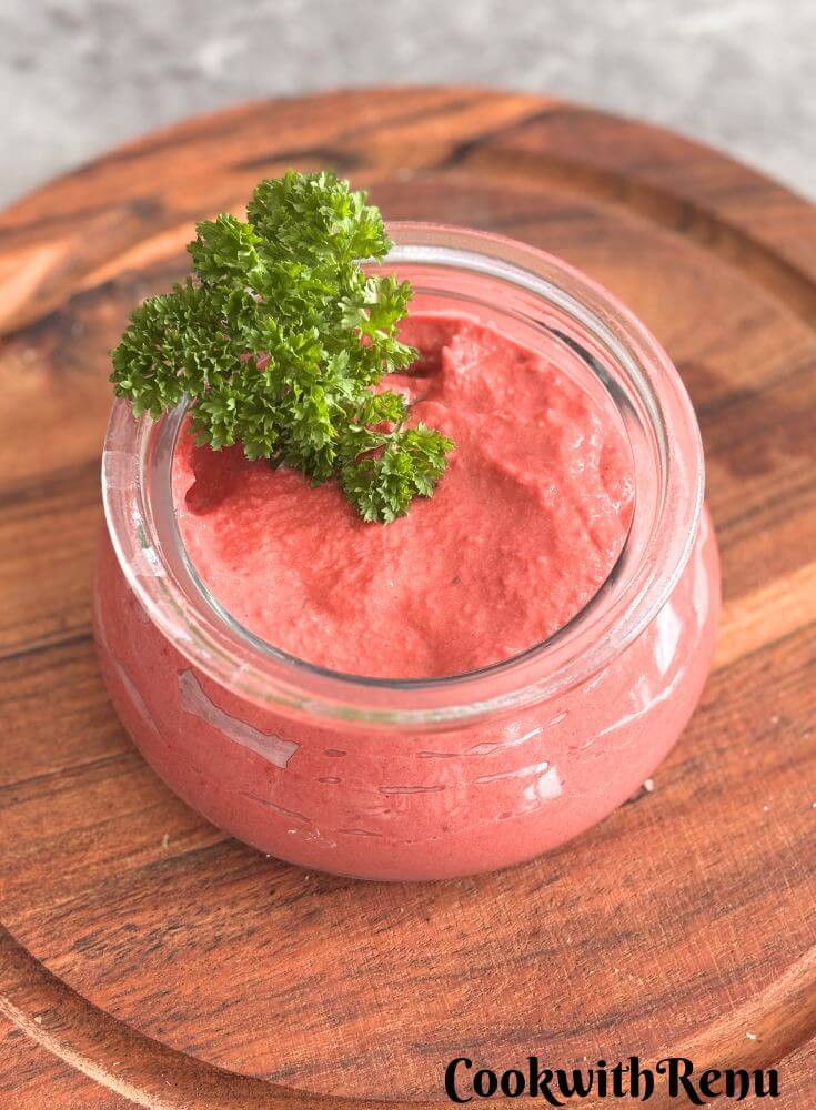 Butter beans, beetroot hummus served in a glass bowl with a garnish of parsley.