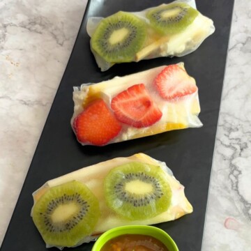 Three Fruit Summer Rolls served on a black tray and some mango chili sauce as a dip.
