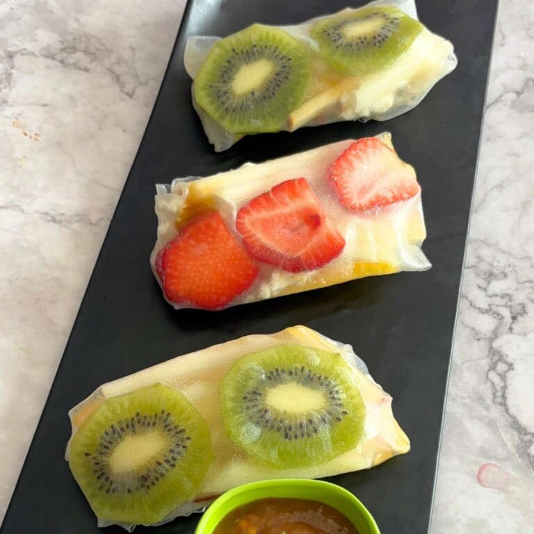 Three Fruit Summer Rolls served on a black tray and some mango chili sauce as a dip.