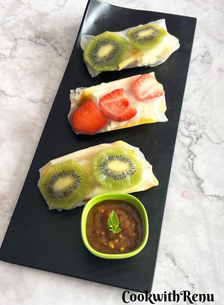 Three Fruit Summer Rolls served on a black tray and some mango chili sauce as a dip.