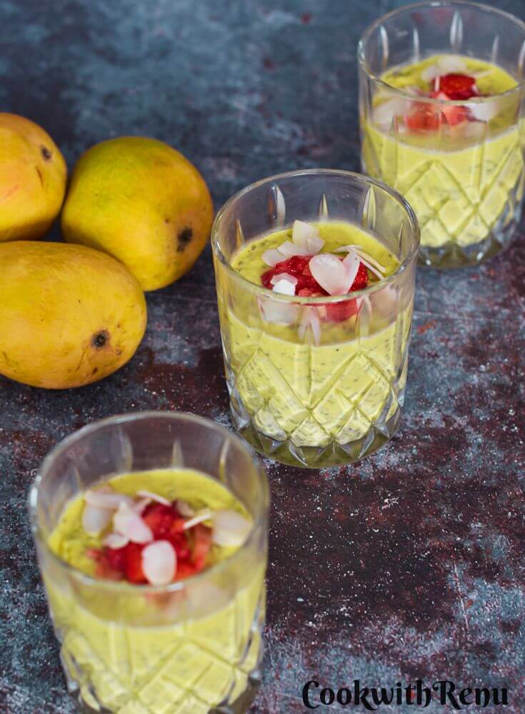 Vegan Mango Chia Seed Pudding served in 3 glasses with a garnish or nuts and strawberry pieces. Seen in the background are some mangoes.