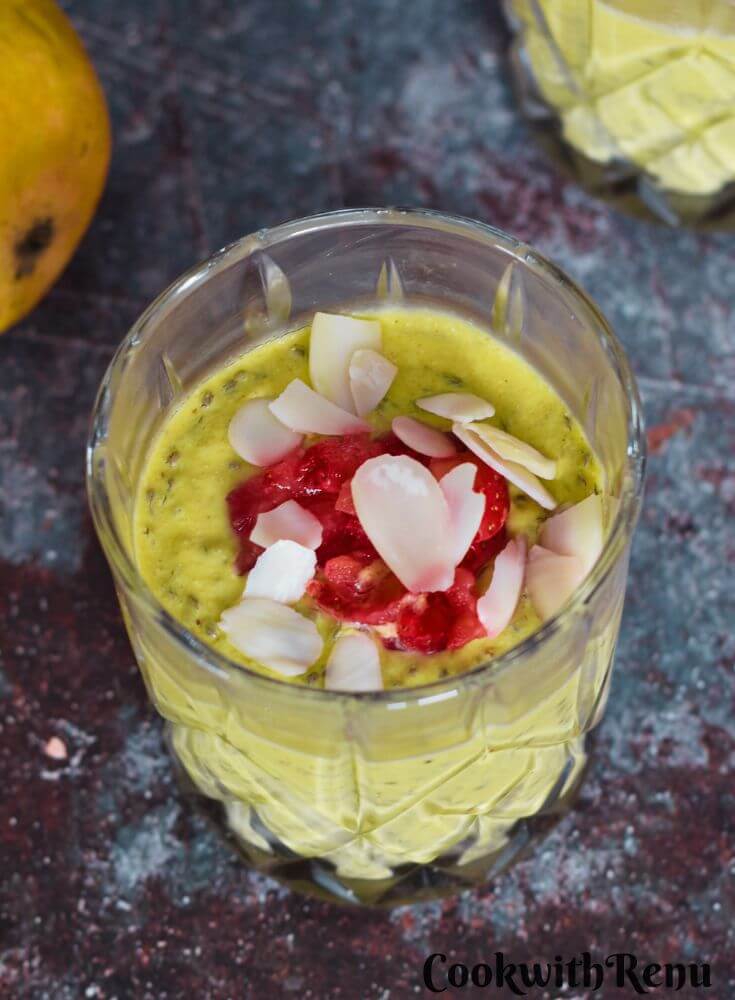 Vegan Mango Chia Seed Pudding served in 3 glasses with a garnish or nuts and strawberry pieces. Seen in the background are some mangoes.