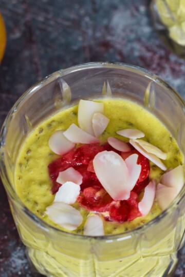 Vegan Mango Chia Seed Pudding served in 3 glasses with a garnish or nuts and strawberry pieces. Seen in the background are some mangoes.