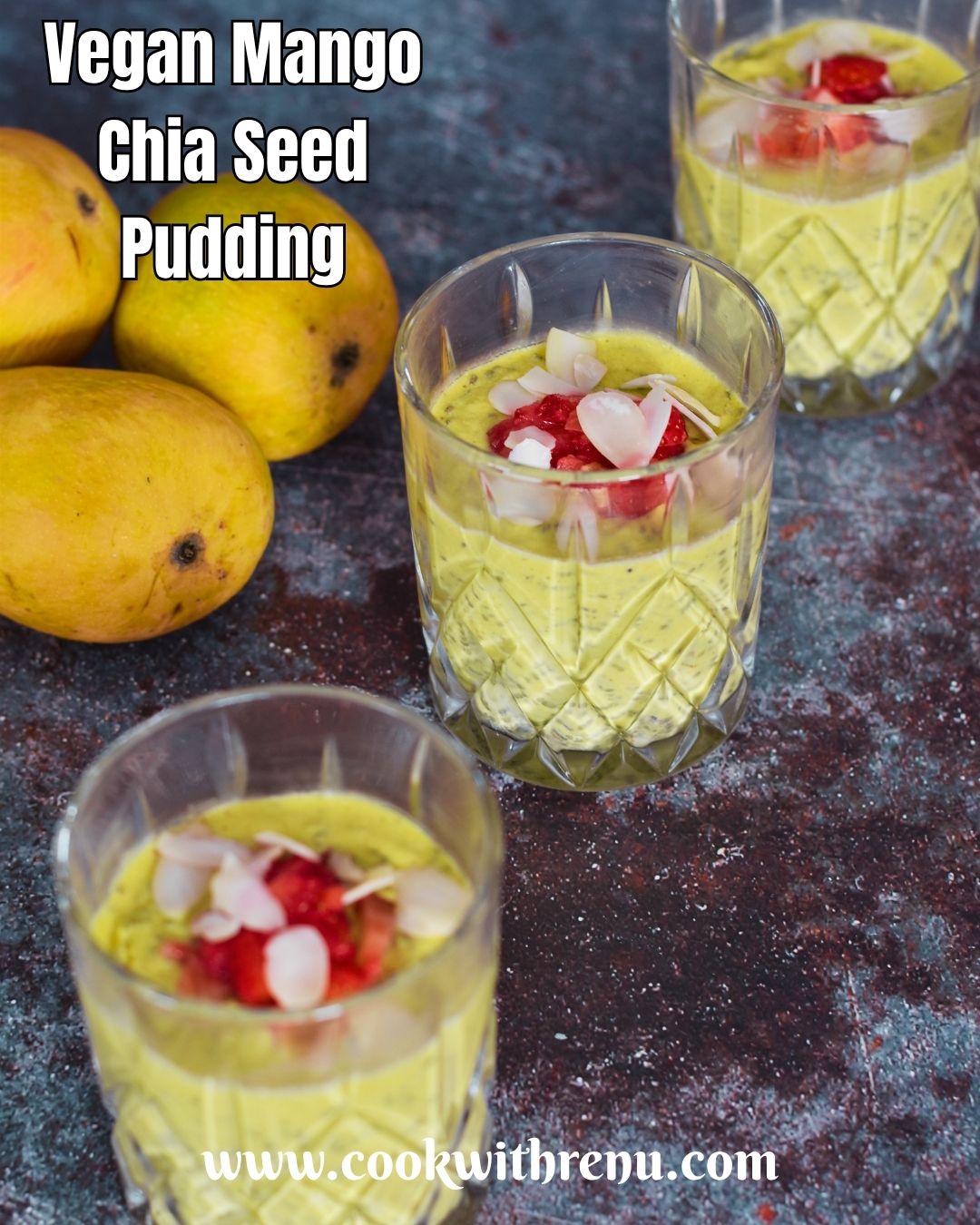 Vegan Mango Chia Seed Pudding served in 3 glasses with a garnish or nuts and strawberry pieces. Seen in the background are some mangoes.