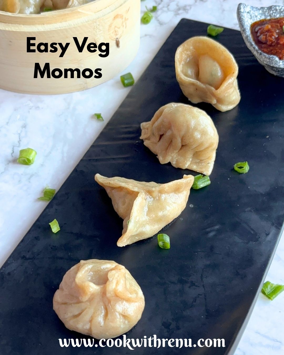 Veg Momos are arranged on a black tray along with spicy garlic chutney. Seen in the background is momos basket with momos in it.