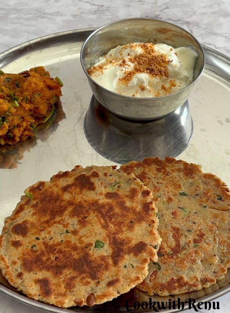 Close up look of Rajgira Paneer Paratha, with yogurt and sweet potato sabji in a steel thali.