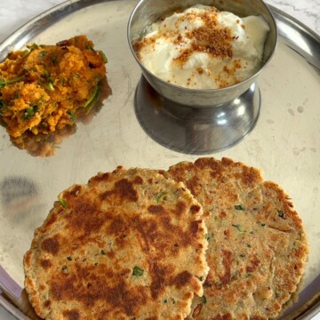 Close up look of Rajgira Paneer Paratha, with yogurt and sweet potato sabji in a steel thali.