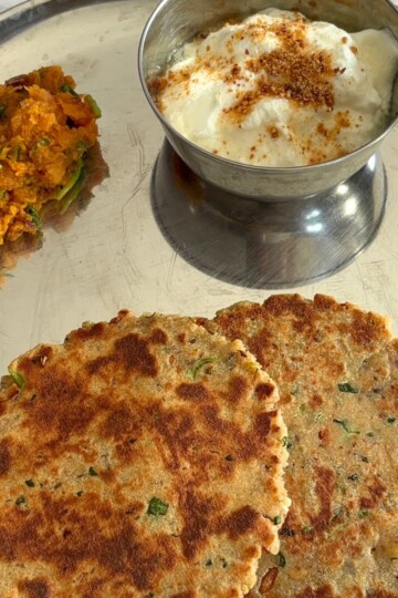Close up look of Rajgira Paneer Paratha, with yogurt and sweet potato sabji in a steel thali.