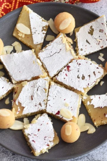 Almond Flour Burfi and Ladoo are arranged on a grey plate, with a red dupatta in the background.