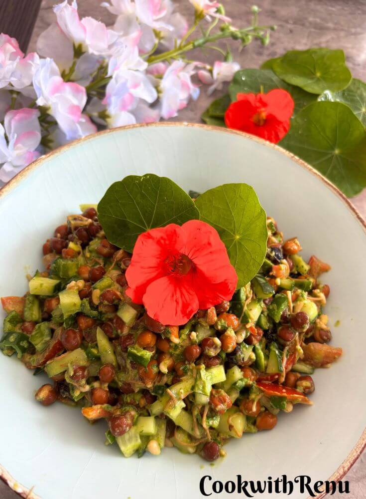 Sprouted Black Chana Salad With Nasturtium Yogurt Dressing, served in a sky-coloured bowl with golden lining and a garnish of nasturtium leaves and flowers. Seen in the background are some nasturtium leaves and flowers.