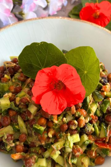 Sprouted Black Chana Salad With Nasturtium Yogurt Dressing, served in a sky-coloured bowl with golden lining and a garnish of nasturtium leaves and flowers. Seen in the background are some nasturtium leaves and flowers.