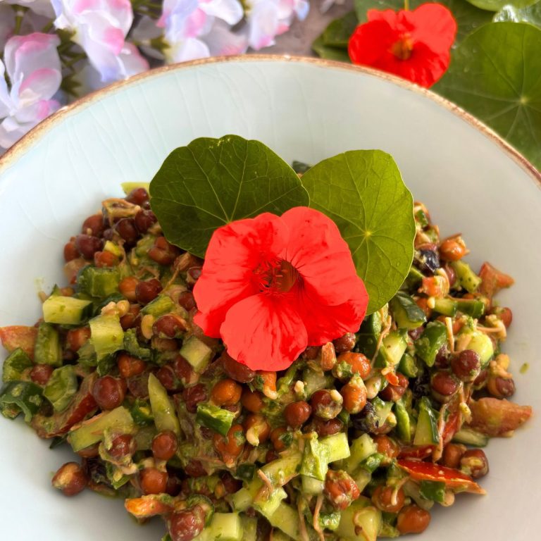 Sprouted Black Chana Salad With Nasturtium Yogurt Dressing, served in a sky-coloured bowl with golden lining and a garnish of nasturtium leaves and flowers. Seen in the background are some nasturtium leaves and flowers.