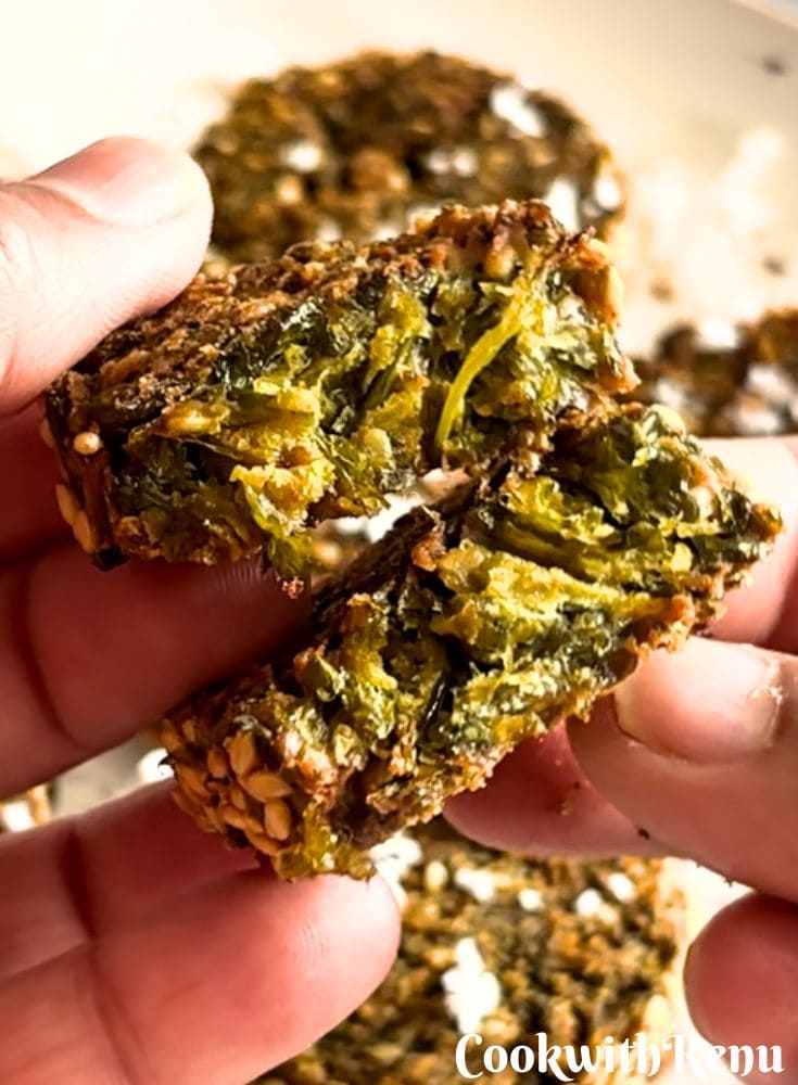 A cut piece of Kothimbir Vadi is held in hand to reveal the internal texture.
