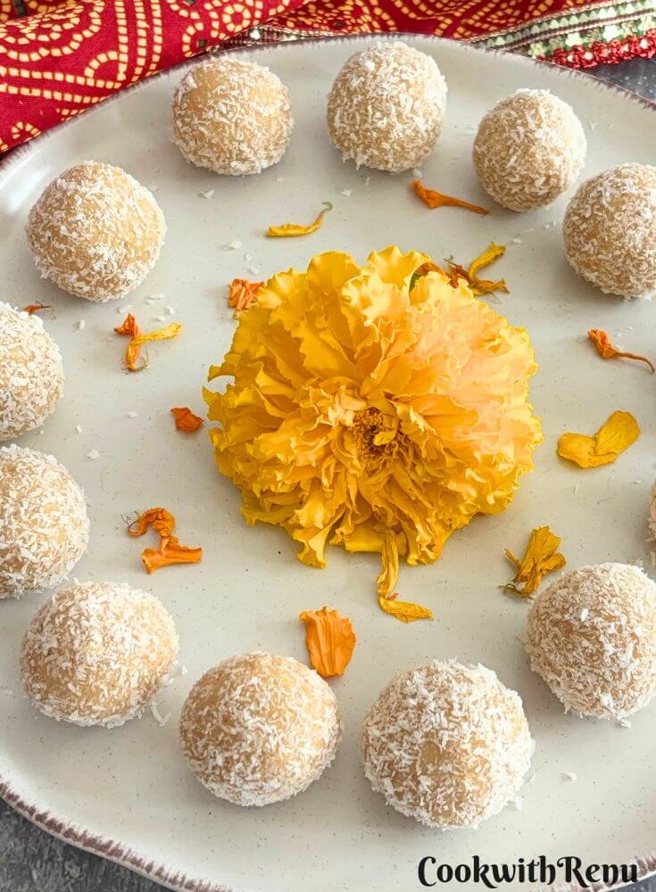 Ladoos arranged on a cream plate with a brown lining and some marigold flowers are seen in the middle.