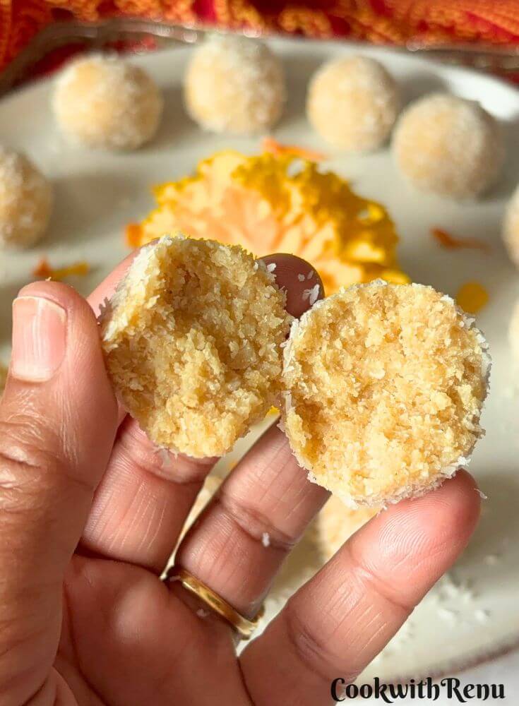 Coconut Ladoo being cut into half and the inside texture is seen along with a lot of ladoos in the background.