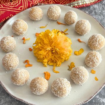 Ladoos arranged on a cream plate with a brown lining and some marigold flowers are seen in the middle.