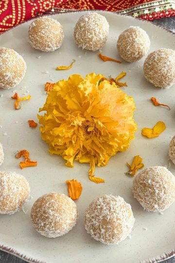 Ladoos arranged on a cream plate with a brown lining and some marigold flowers are seen in the middle.